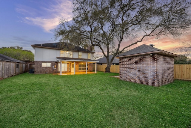 rear view of property featuring brick siding, a fenced backyard, and a lawn