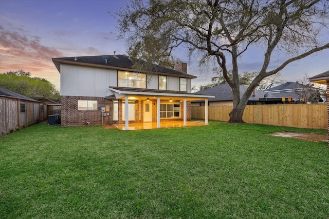 back of house at dusk with a yard, brick siding, central AC unit, and a fenced backyard