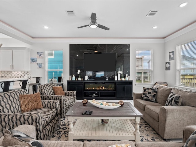 living room with visible vents, recessed lighting, a glass covered fireplace, and ornamental molding