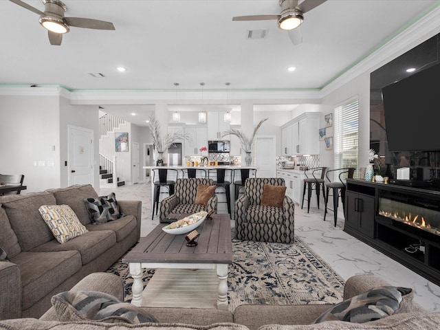 living room with visible vents, stairs, a glass covered fireplace, marble finish floor, and a ceiling fan