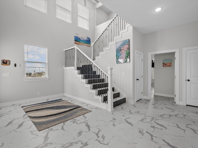 stairway with recessed lighting, baseboards, marble finish floor, and a towering ceiling