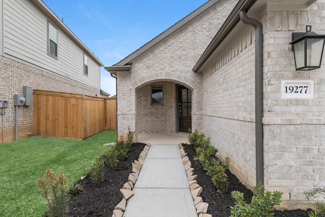 doorway to property featuring fence, brick siding, and a lawn