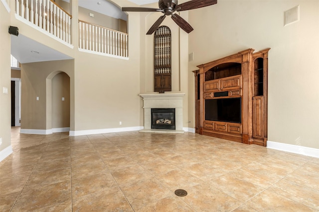 unfurnished living room featuring baseboards, arched walkways, ceiling fan, and a tiled fireplace