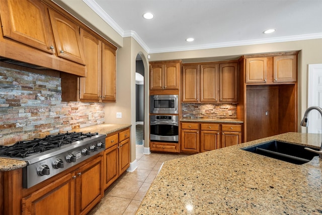 kitchen with light tile patterned floors, light stone countertops, a sink, appliances with stainless steel finishes, and brown cabinets