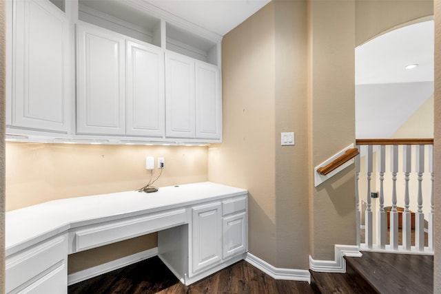 unfurnished office featuring dark wood-style floors, baseboards, built in desk, and arched walkways