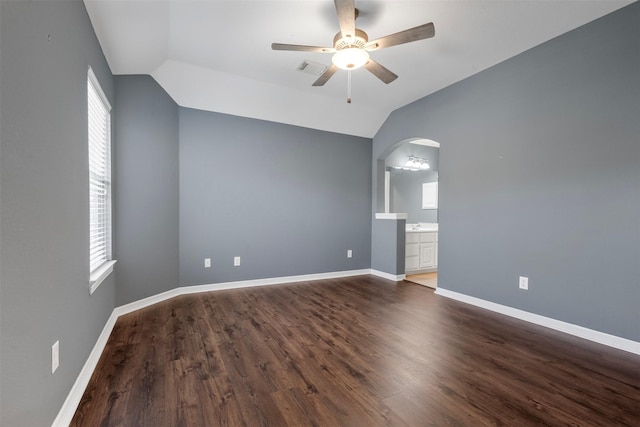 spare room with baseboards, dark wood finished floors, vaulted ceiling, arched walkways, and a ceiling fan