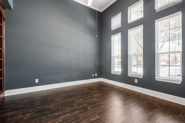 unfurnished room with crown molding, baseboards, and dark wood-style flooring