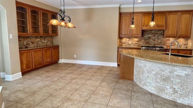 kitchen with ornamental molding, a sink, light stone counters, brown cabinetry, and baseboards