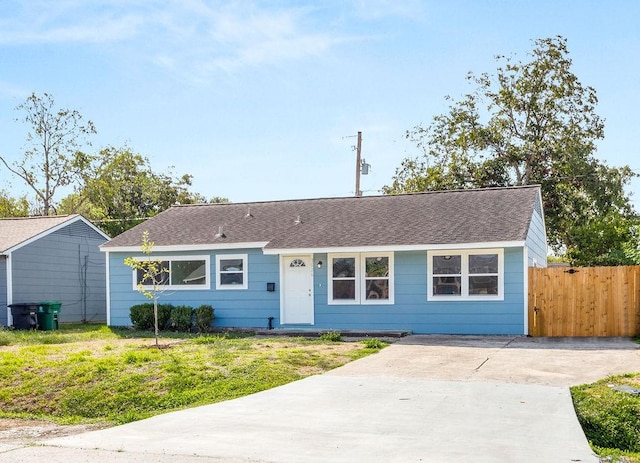 ranch-style home with a shingled roof, a front yard, and fence