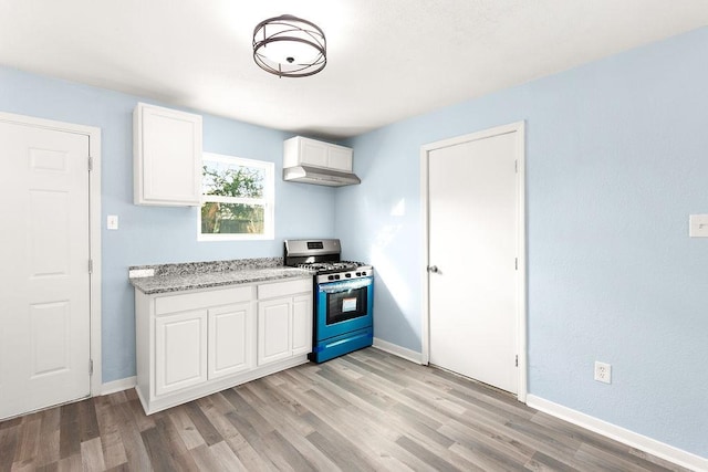 kitchen with light wood-style flooring, light stone counters, stainless steel range with gas cooktop, white cabinets, and baseboards