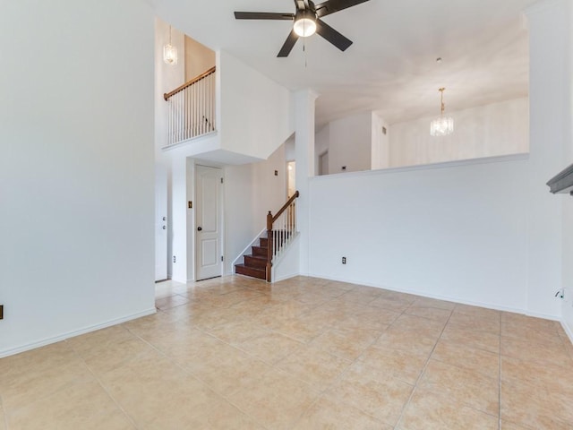 tiled empty room with stairs, a high ceiling, ceiling fan with notable chandelier, and baseboards