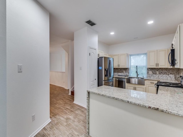 kitchen with visible vents, a sink, appliances with stainless steel finishes, decorative backsplash, and light stone countertops