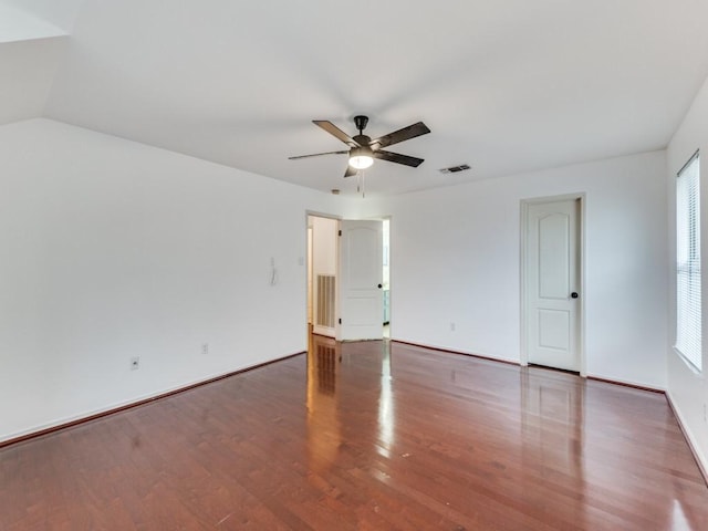 empty room with visible vents, baseboards, ceiling fan, vaulted ceiling, and wood finished floors