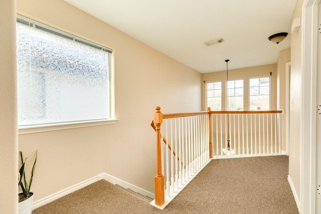 hallway featuring visible vents, carpet floors, baseboards, and an upstairs landing