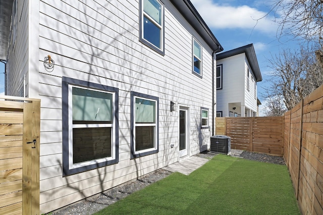 back of house with cooling unit, a lawn, and a fenced backyard