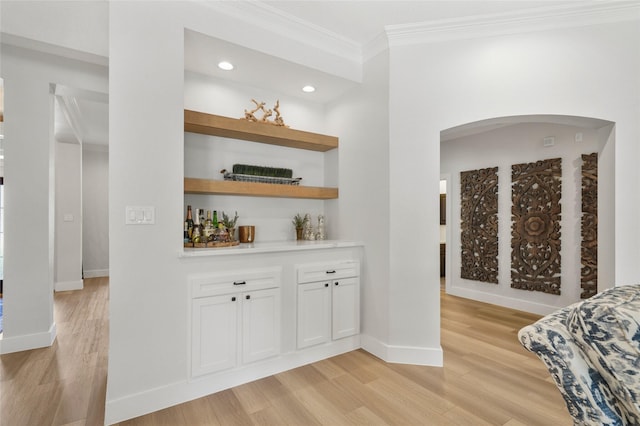 bar with crown molding, baseboards, light wood-type flooring, arched walkways, and a bar