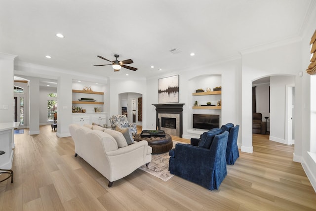 living area featuring a tiled fireplace, light wood-style flooring, built in shelves, and baseboards