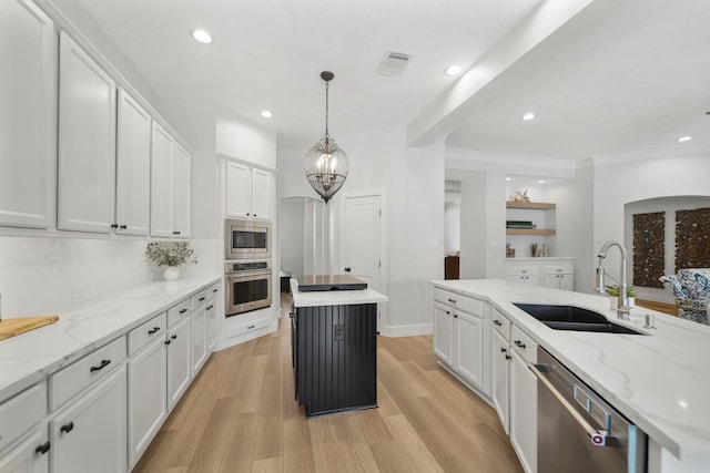 kitchen with a kitchen island, light wood-style flooring, white cabinets, stainless steel appliances, and a sink