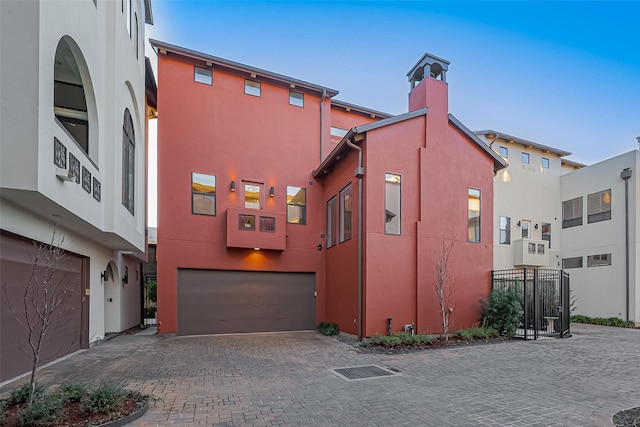 exterior space with stucco siding, a chimney, decorative driveway, and a garage