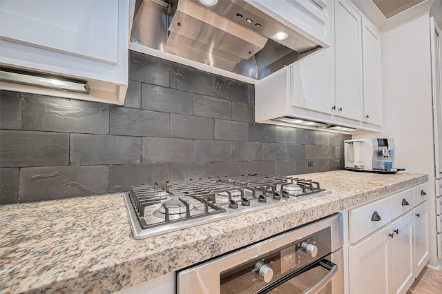 kitchen with wall oven, stainless steel gas stovetop, white cabinets, decorative backsplash, and extractor fan