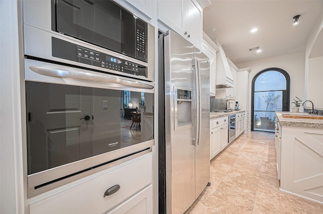 kitchen featuring premium range hood, a sink, decorative backsplash, white cabinets, and appliances with stainless steel finishes