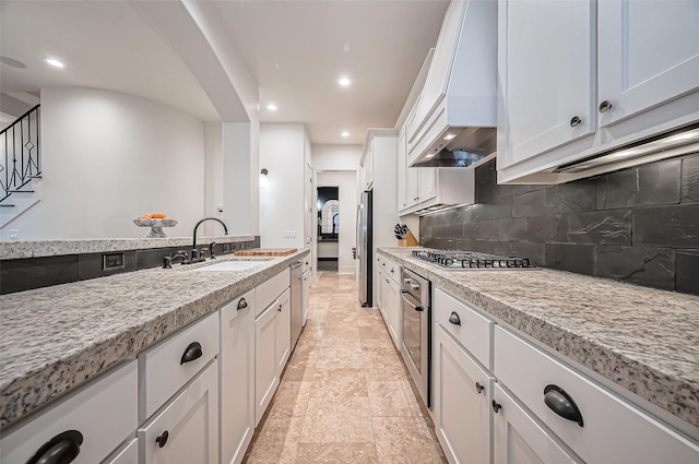 kitchen featuring custom range hood, a sink, tasteful backsplash, appliances with stainless steel finishes, and white cabinets