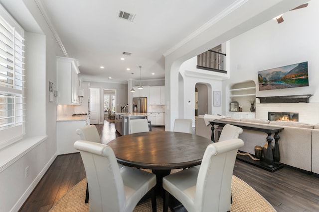 dining area featuring visible vents, dark wood finished floors, ornamental molding, arched walkways, and a glass covered fireplace