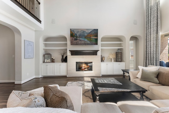 living room featuring arched walkways, dark wood finished floors, a tiled fireplace, and built in shelves