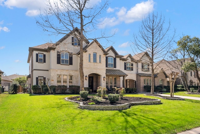 french country home featuring stone siding, a front lawn, and fence