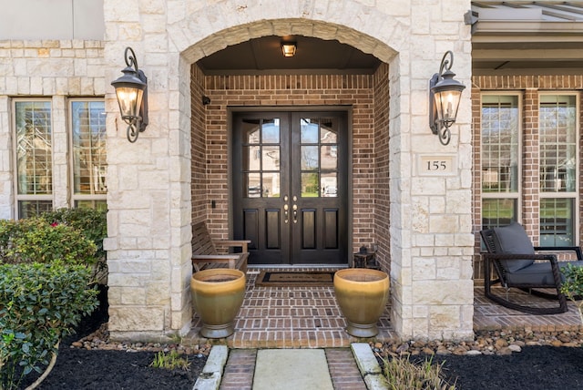 doorway to property featuring brick siding, stone siding, and french doors