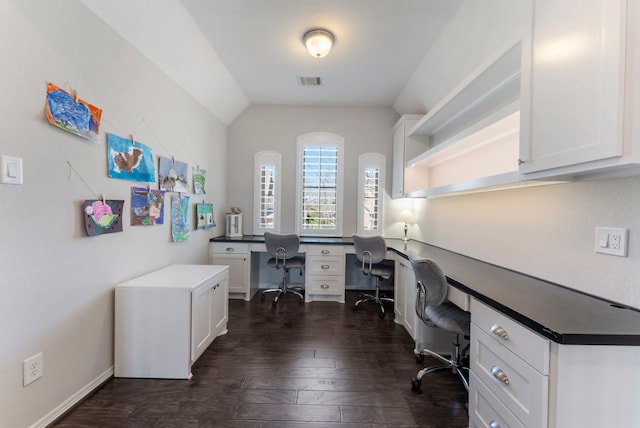 office featuring vaulted ceiling, visible vents, dark wood-style flooring, and built in study area