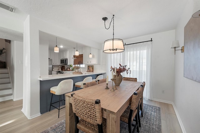 dining room featuring visible vents, light wood-type flooring, stairs, and baseboards