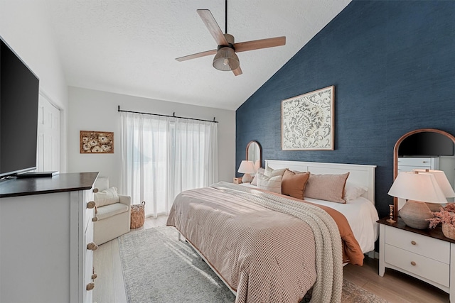 bedroom featuring wallpapered walls, vaulted ceiling, light wood-style floors, a textured ceiling, and an accent wall