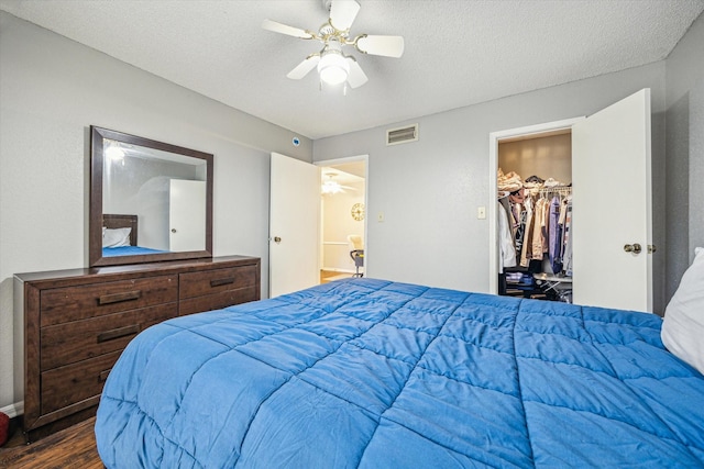 bedroom with a spacious closet, visible vents, wood finished floors, a textured ceiling, and a ceiling fan