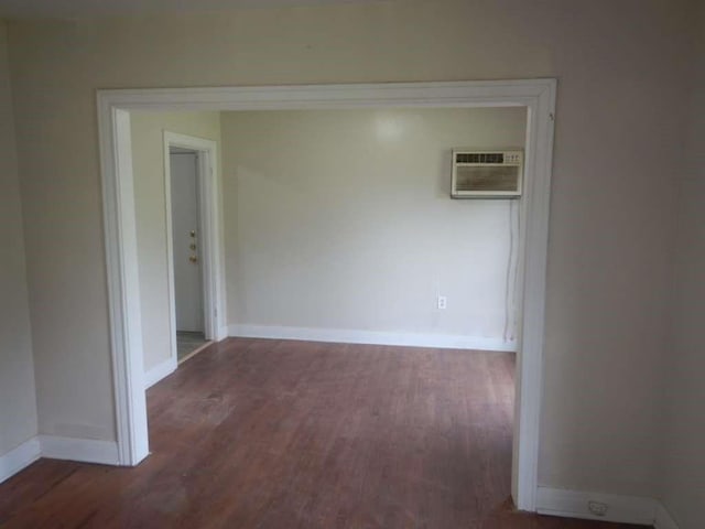 spare room featuring baseboards, a wall unit AC, and wood finished floors