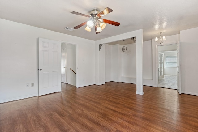 empty room featuring visible vents, baseboards, wood finished floors, and ceiling fan with notable chandelier