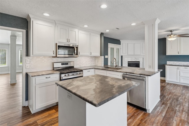 kitchen featuring a sink, appliances with stainless steel finishes, a peninsula, white cabinets, and decorative columns