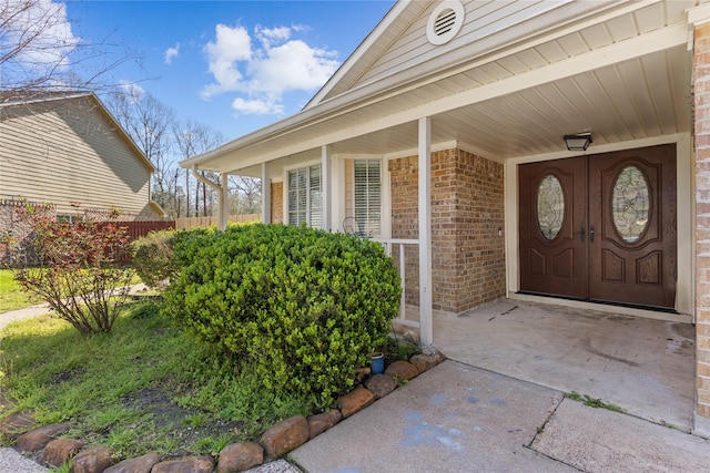 view of exterior entry featuring brick siding, covered porch, and fence