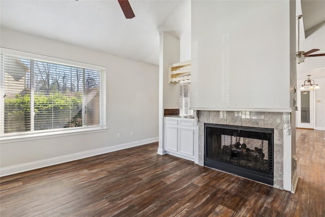 unfurnished living room featuring baseboards, a tile fireplace, dark wood-style flooring, and ceiling fan