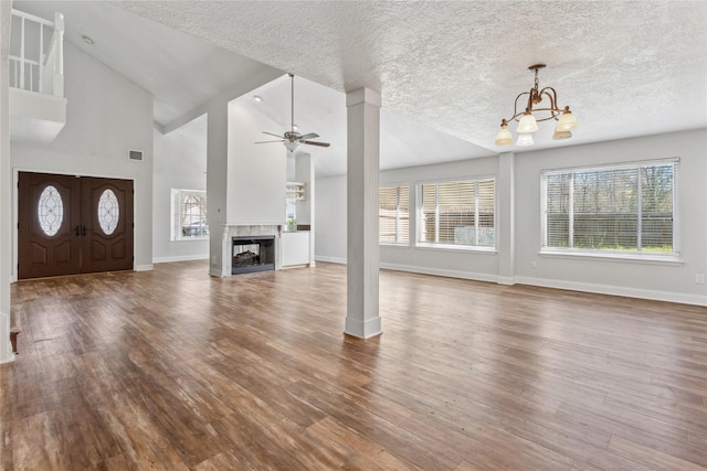 unfurnished living room with visible vents, ceiling fan with notable chandelier, wood finished floors, baseboards, and a multi sided fireplace