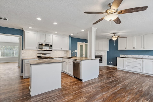 kitchen with a peninsula, dark wood-type flooring, white cabinets, appliances with stainless steel finishes, and backsplash