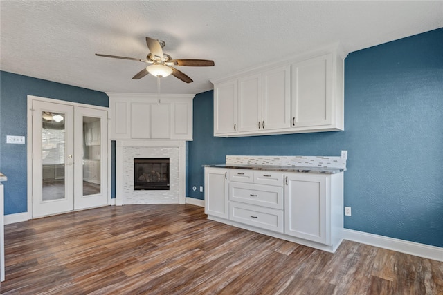 kitchen with a glass covered fireplace, white cabinets, wood finished floors, and a textured ceiling