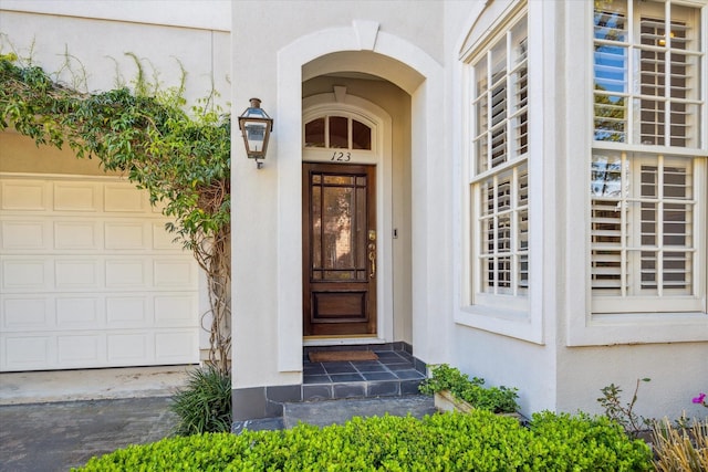 view of exterior entry with a garage and stucco siding