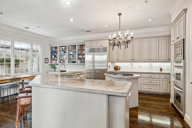 kitchen featuring dark wood-type flooring, an island with sink, built in appliances, and a sink