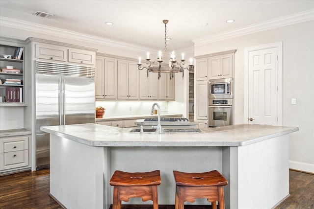 kitchen featuring visible vents, built in appliances, dark wood-style floors, and a center island with sink