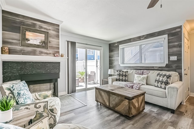 living area with a ceiling fan, wood finished floors, a fireplace, and ornamental molding