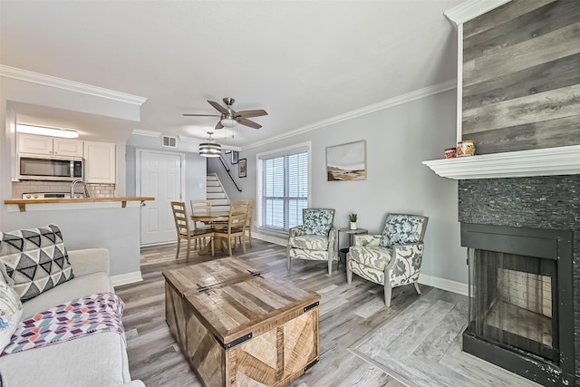 living area with visible vents, baseboards, a fireplace, ornamental molding, and light wood-style floors