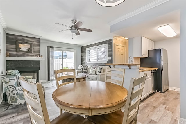 dining area featuring baseboards, light wood-style flooring, ceiling fan, ornamental molding, and a glass covered fireplace