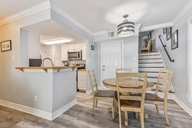 dining room featuring visible vents, baseboards, crown molding, and light wood-style floors