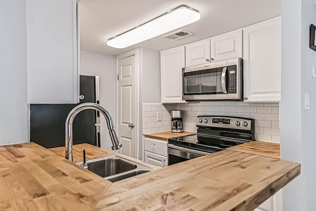 kitchen with visible vents, butcher block countertops, decorative backsplash, stainless steel appliances, and a sink